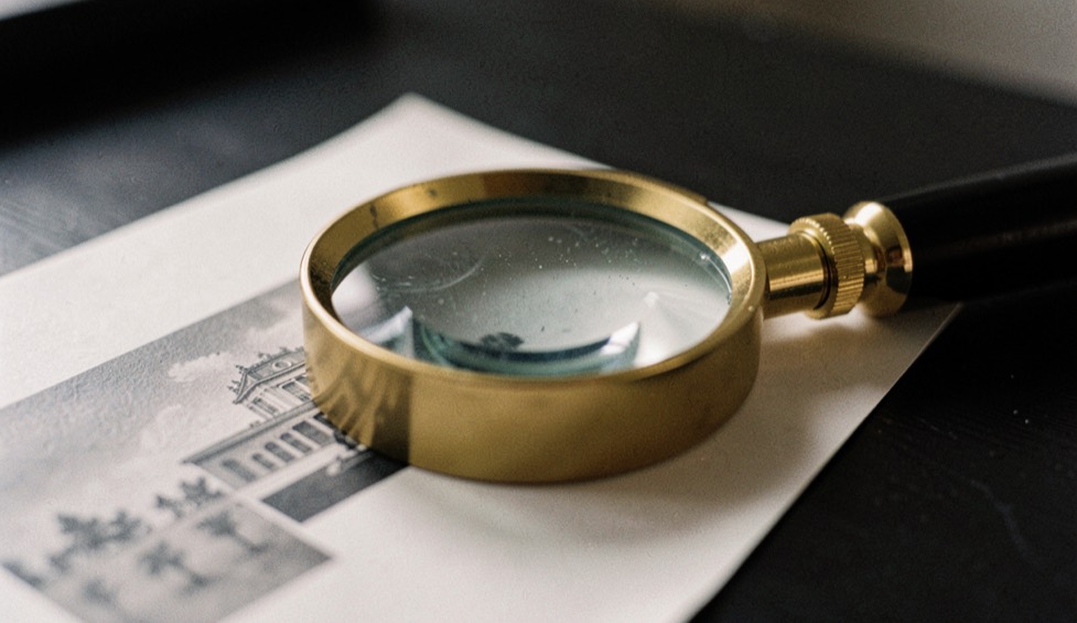 Une loupe de typographe posée sur un tirage papier, grain de l’image visible à travers la lentille, table sombre, lumière dirigée, macro.